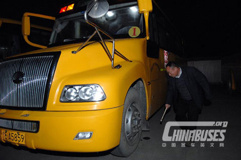 Driver Tang Zhiqiang checks the tyre of a school bus in Deqing County